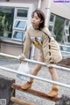 A woman in a beige sweatshirt and shorts is standing on a railing.