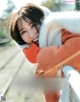 A woman in an orange sweater and white fur coat posing for a magazine.