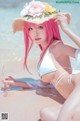 A woman with pink hair wearing a straw hat on the beach.