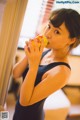 A woman in a black dress drinking from a yellow cup.