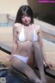 A woman in a white bikini sitting by a pool.